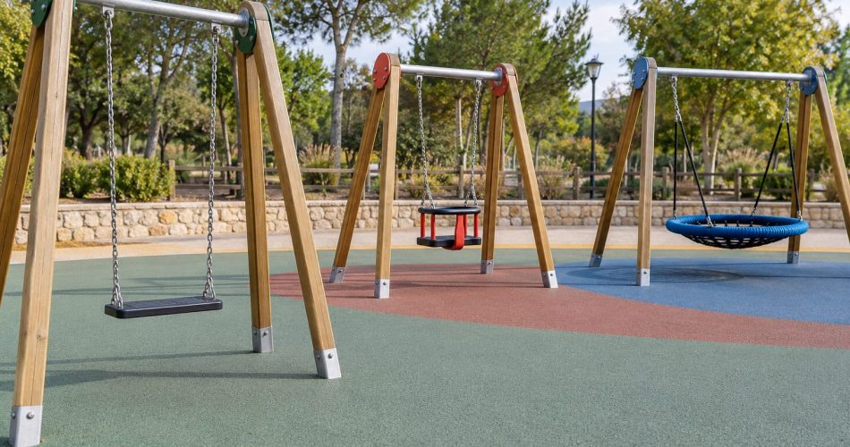 Columpios de asiento plano, cesta y tipo nido en un parque infantil con pavimento amortiguador.